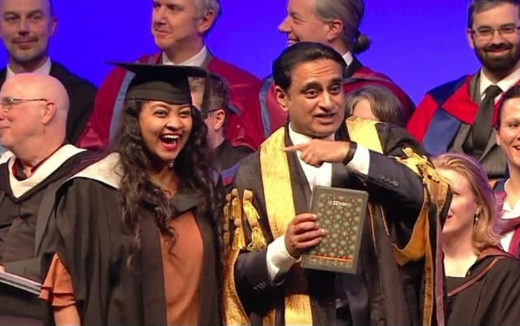 Tanjila Mazumder Drishti standing next to the University's Chancellor Sanjeev Bhaskar OBE who is pointing at her as she crosses the stage in her graduation gown.