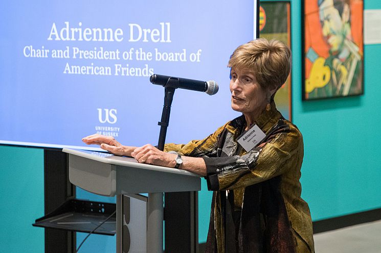 Adrienne Drell, Chair and President of the American Friends standing at a lectern speaking in front of a screen