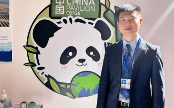 Dr Yushi Chen stood in front of the sign for the China Pavilion at COP 28 wearing a suit and lanyard.