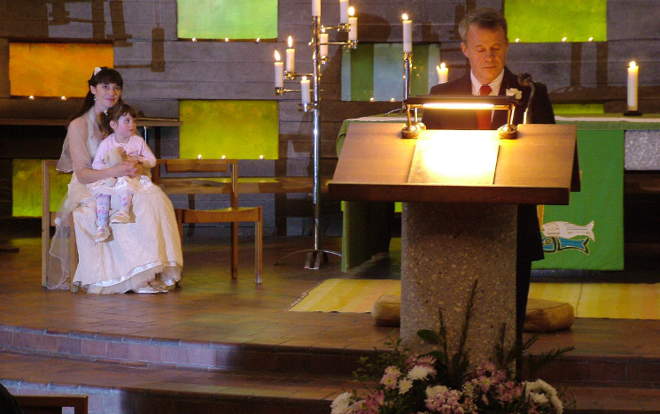 Jeremy reading a poem, while Alexandra sits with their daughter on her lap during their wedding ceremony in the Meeting House. Photographer: Strat Mastoris