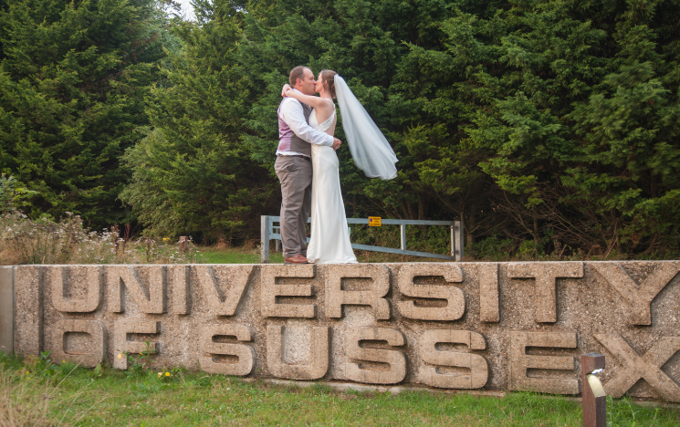 Tom Burnell and Rosie Mulhern stood on top of the University of Sussex concrete sign in their wedding clothes.