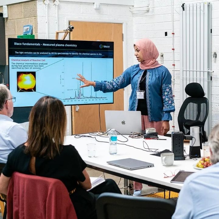 Square Biaco Innovate A woman points at a screen that she is presenting from to a room of people.