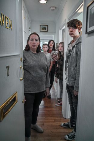 Photograph of an open front door (says 'Haven' on it). The door opens onto a hallway where 7 people (3 women, 1 man, 1 boy, 1 girl) are standing either in a doorway or in the hallway. They are all looking at the open doorway.