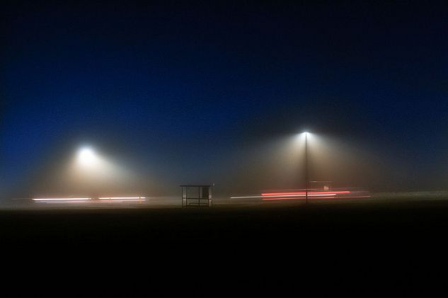 A bus stop and two moving cars on a foggy night