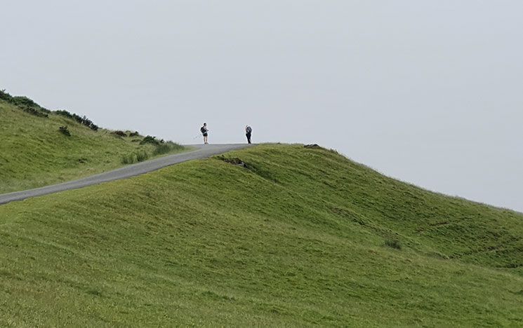 A photo of a green hill, with two men in the distance chatting