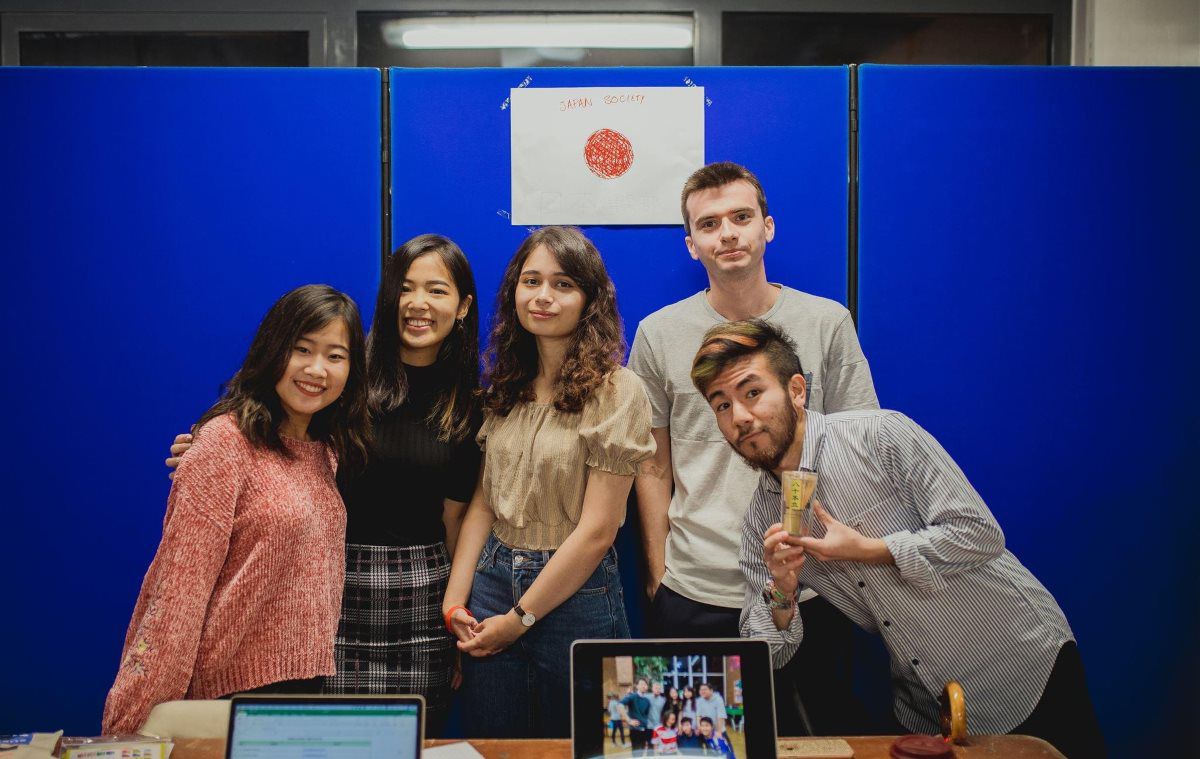 Students at a Fresher's fair smiling at the camera advertising Japanese Society