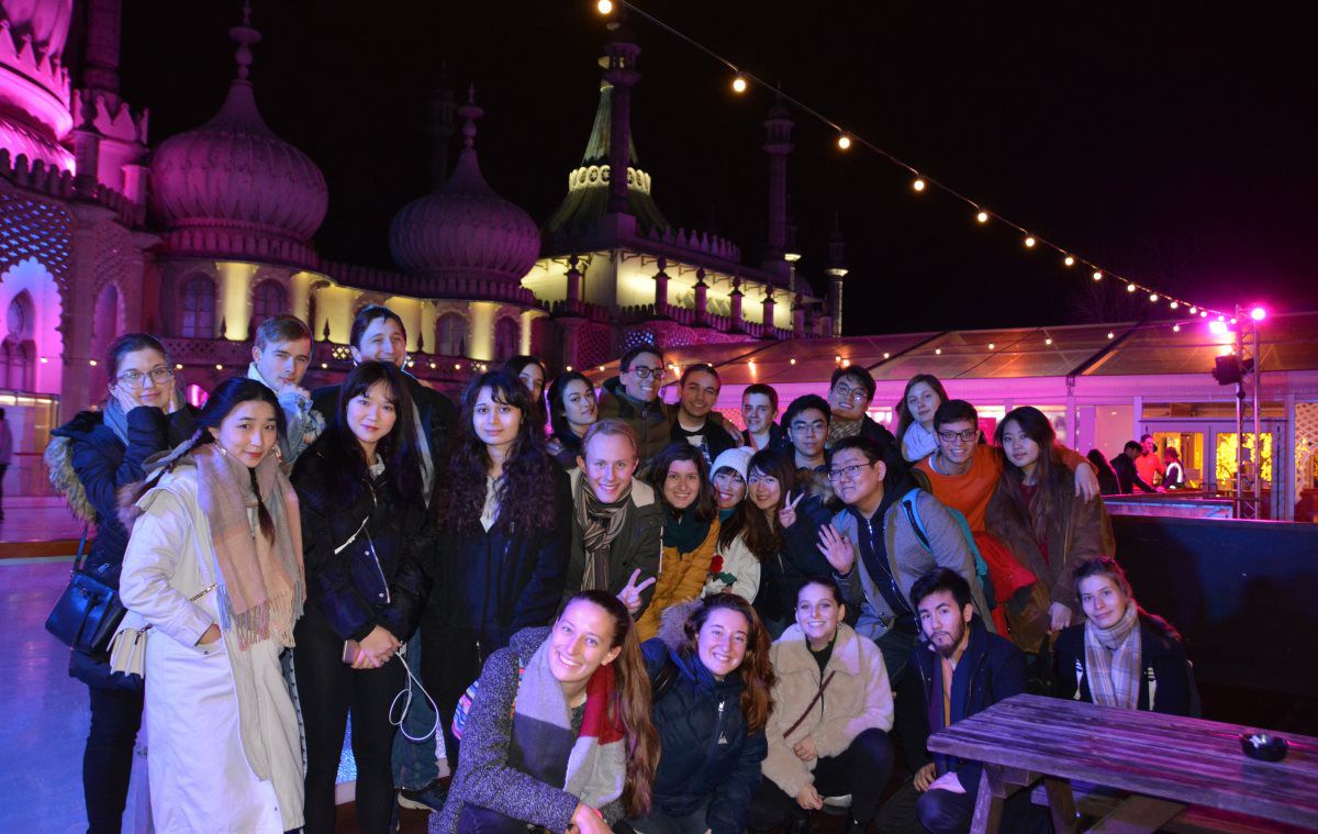 A group of students on an ice rink at night in winter clothing posing for a photo