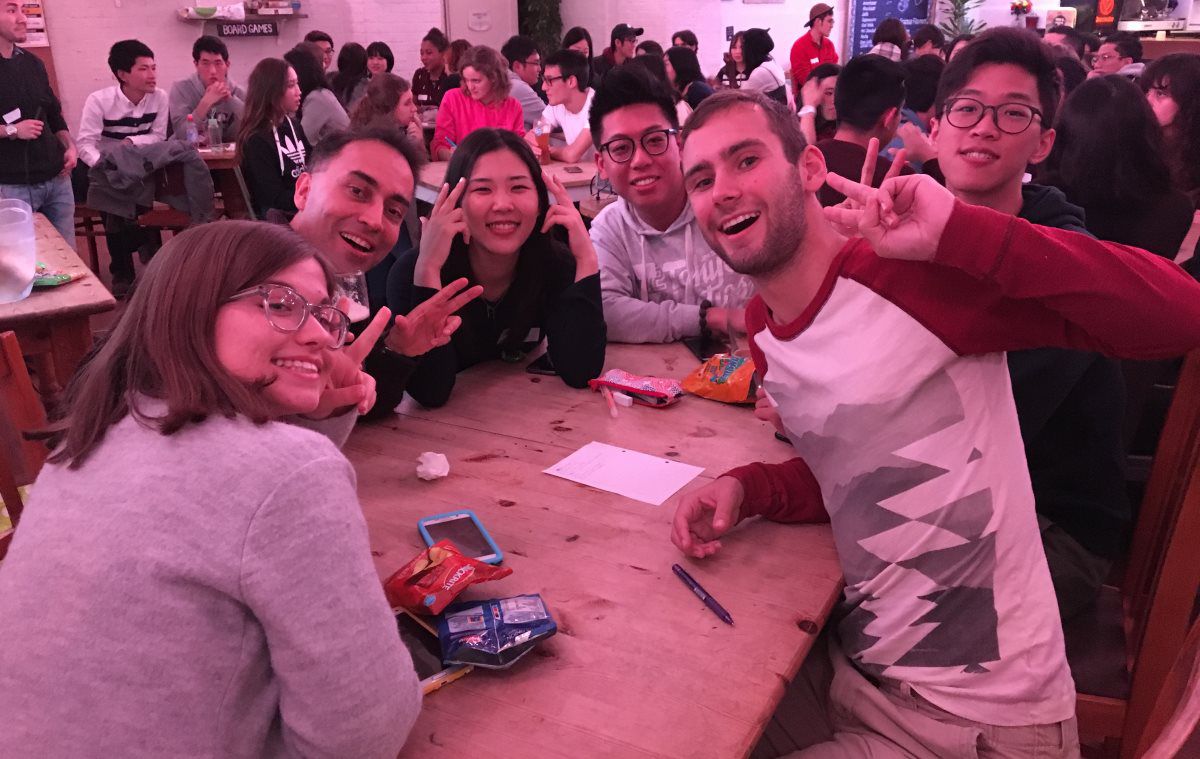 A group of students sit round a table in a bar with a quiz sheet smiling