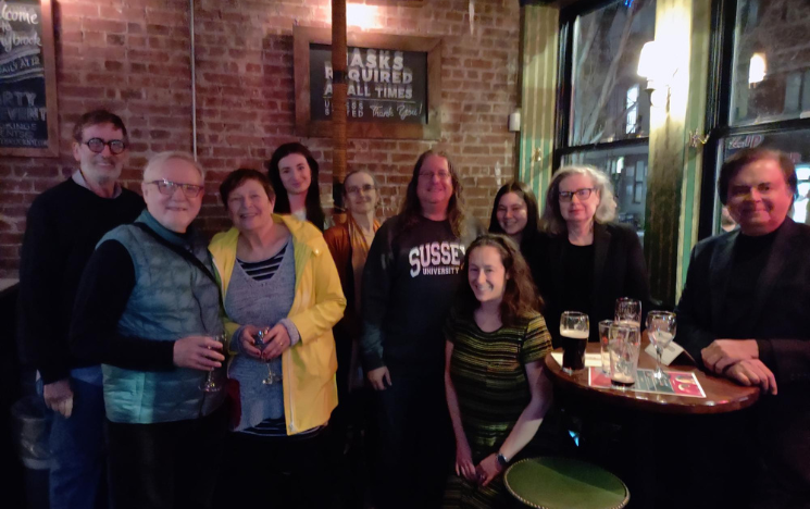 A group of alumni in a bar standing with their backs to a brick wall and smiling