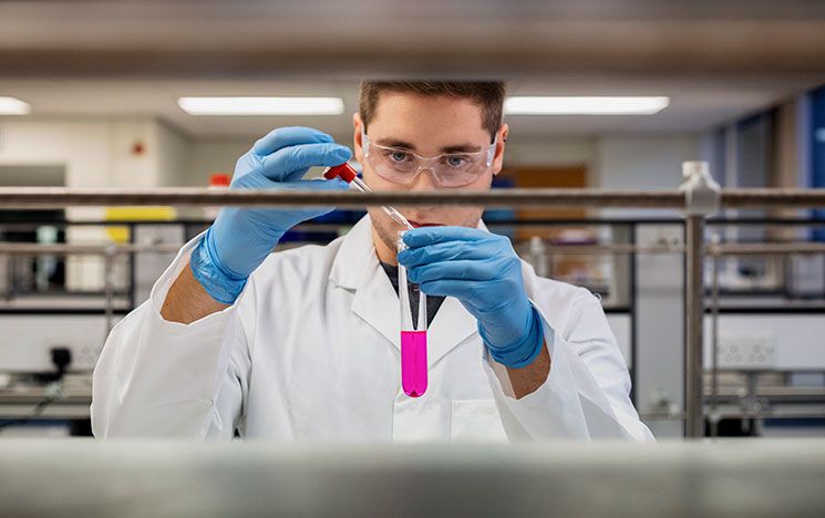 A student working in a lab, holding a glass phial and pipette