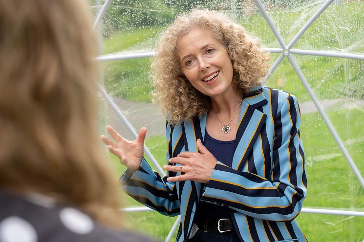 Professor Michelle LeFevre standing inside an outdoor structure gesturing as she speaks to a listener