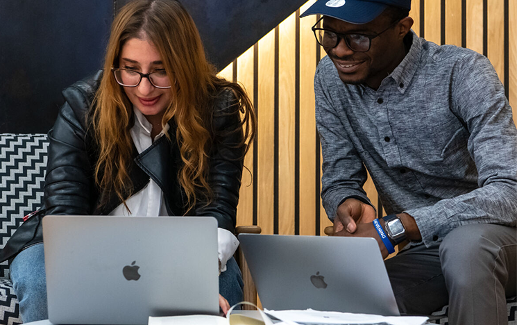 Two students sitting at a small table studying their laptops